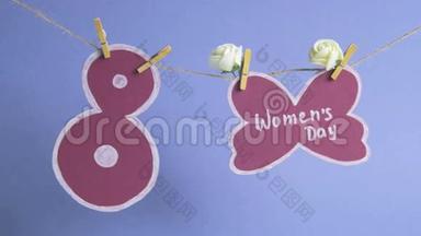妇女节`快乐.. 妇女节`纸上装饰着鲜花，挂在一根绳子上靠近一张纸编号8.. 蓝色背景
